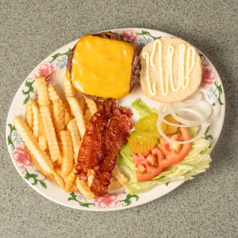 Cheeseburger with melted cheese, crinkle-cut fries, bacon, and a side salad on a floral plate.