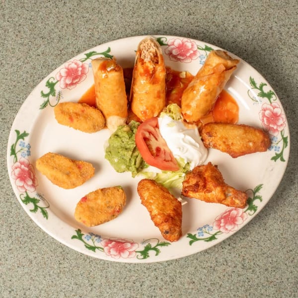Platter of taquitos, chicken wings, fried appetizers, guacamole, sour cream, and tomato.