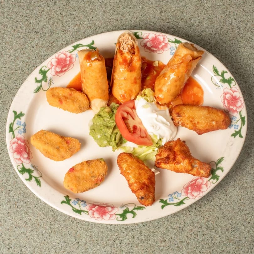 Platter of taquitos, chicken wings, fried appetizers, guacamole, sour cream, and tomato.
