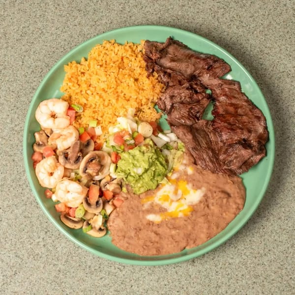 Grilled steak, rice, beans, guacamole, and shrimp with mushrooms on a green plate.