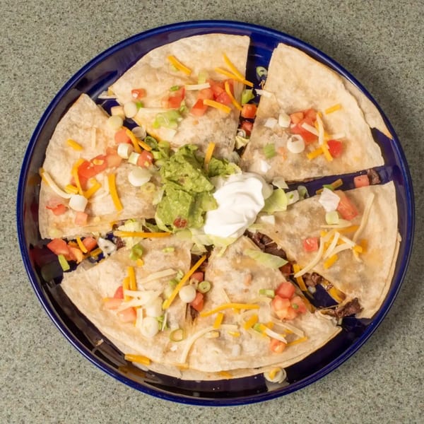 Quesadilla wedges on a blue plate, topped with guacamole, sour cream, cheese, tomatoes, and green onions.