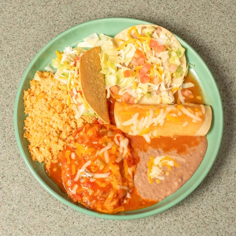 Mexican combo platter with rice, beans, taco, tostada, and enchilada on a green plate.