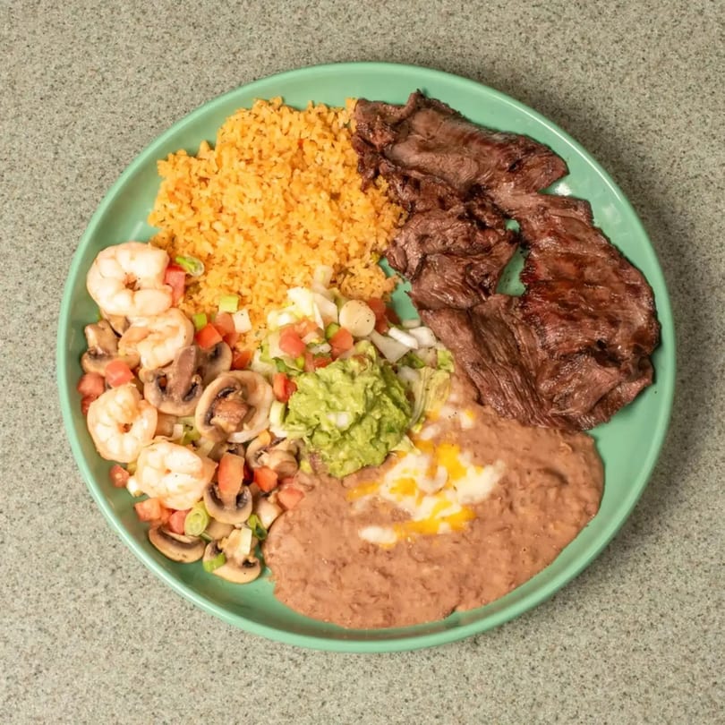Grilled steak, shrimp, rice, refried beans, guacamole, and pico de gallo on a green plate.