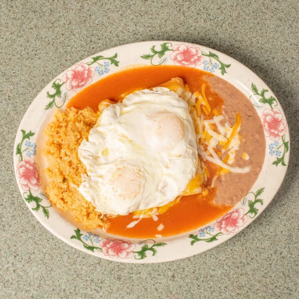 Mexican breakfast plate with two fried eggs, red sauce, cheese, rice, and refried beans.