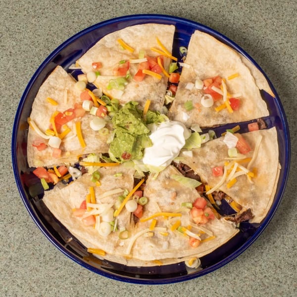 Quesadilla wedges topped with guacamole, sour cream, tomatoes, cheese, and green onions on a blue plate.